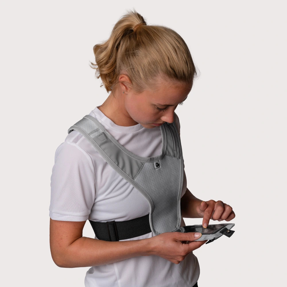 Dette er et billede af en kvinde i en refleks løbevest fra RUNMATE, som anvender sin mobil i mobilholderen