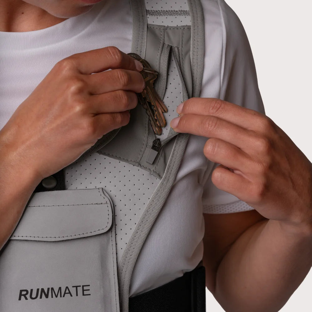 Dette er et billede af en kvinde i en refleks løbevest fra RUNMATE, som lægger sine nøgler i sidelommen på løbevesten