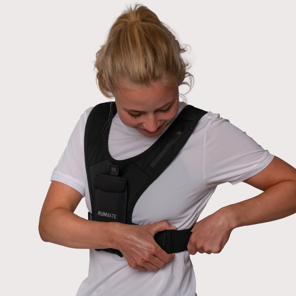 Dette er et billede af en kvinde i en sort løbevest fra RUNMATE, som justerer vesten