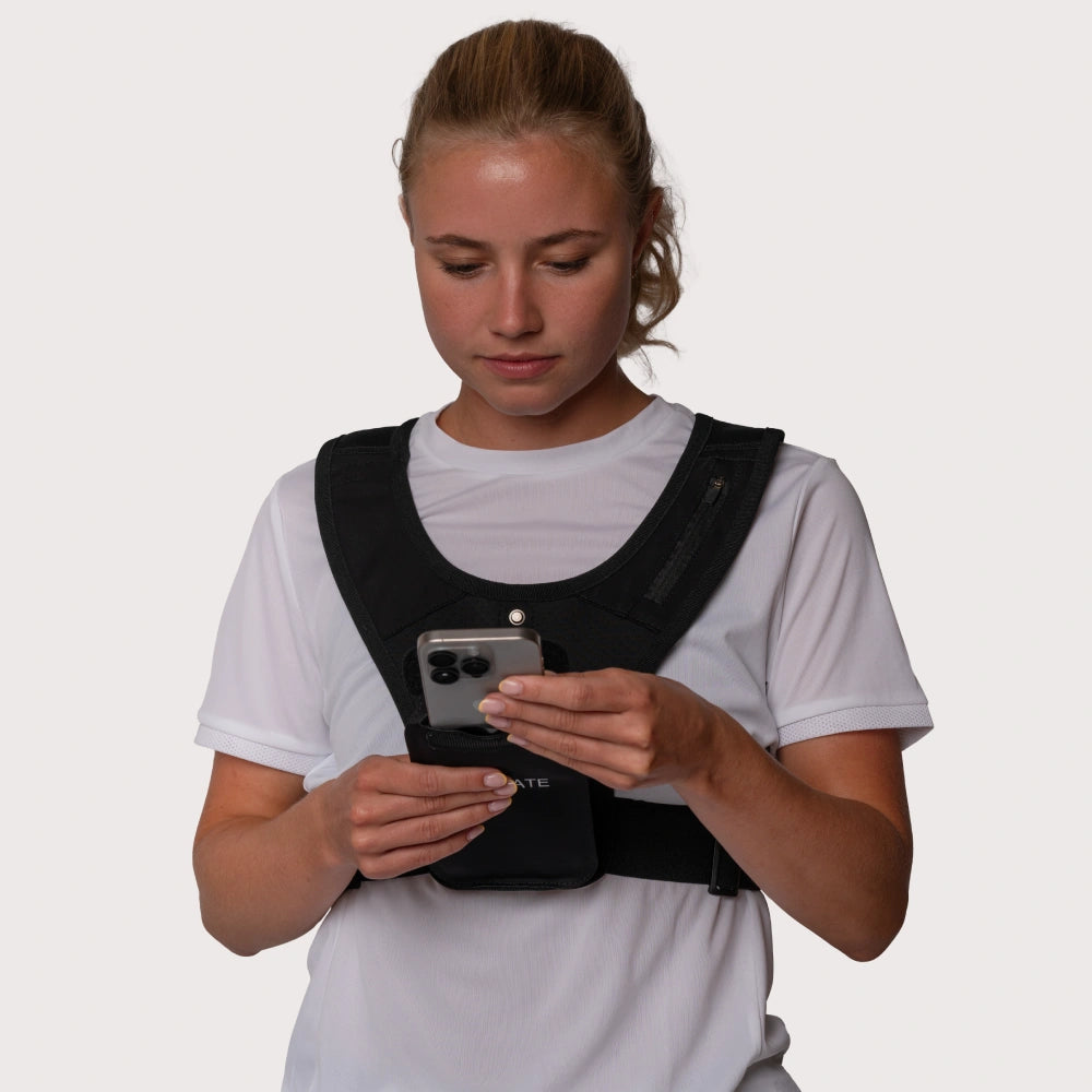Dette er et billede af en kvinde i en sort løbevest fra RUNMATE, som anvender sin mobil i mobilholderen